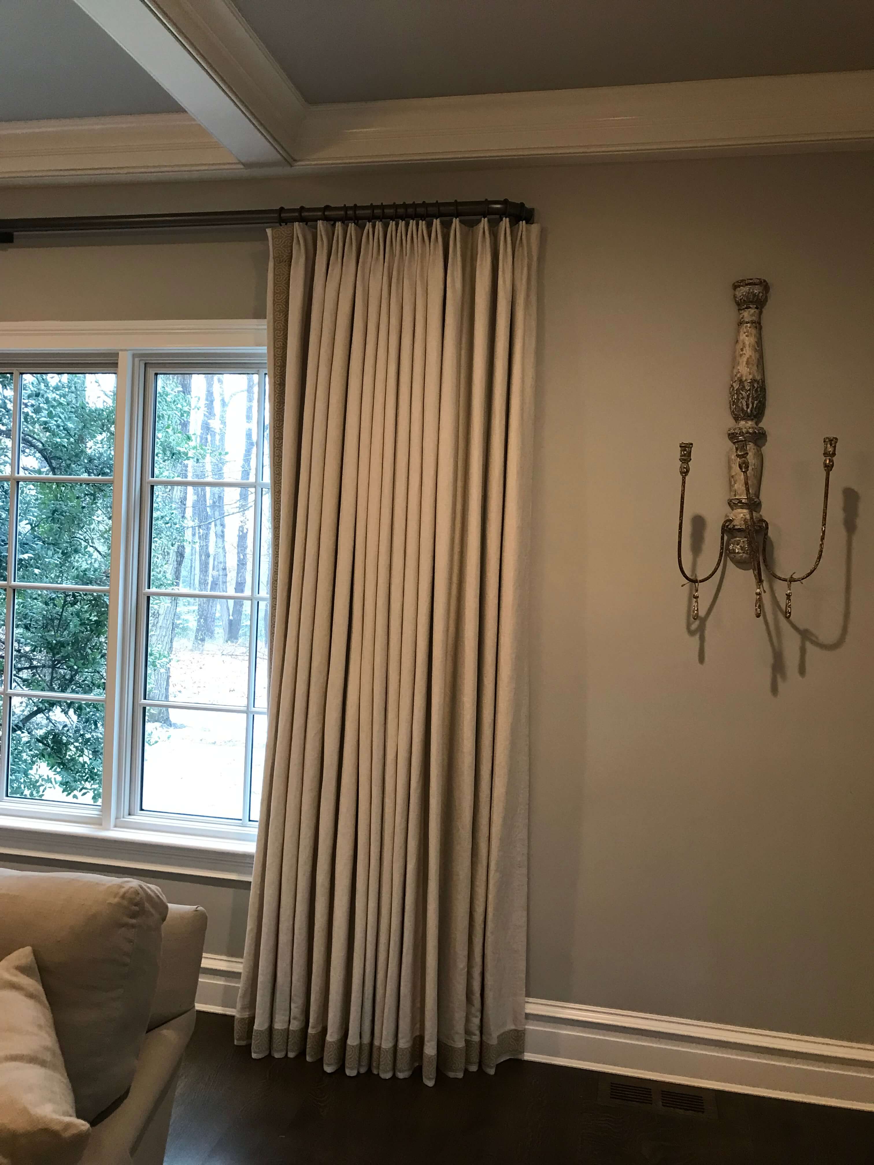 Draperies made out of linen with 3” decorative tape running down the front and across the bottom of the panel. The rod is metal with an elbow bracket which returns back into the wall. This is a very transitional design.