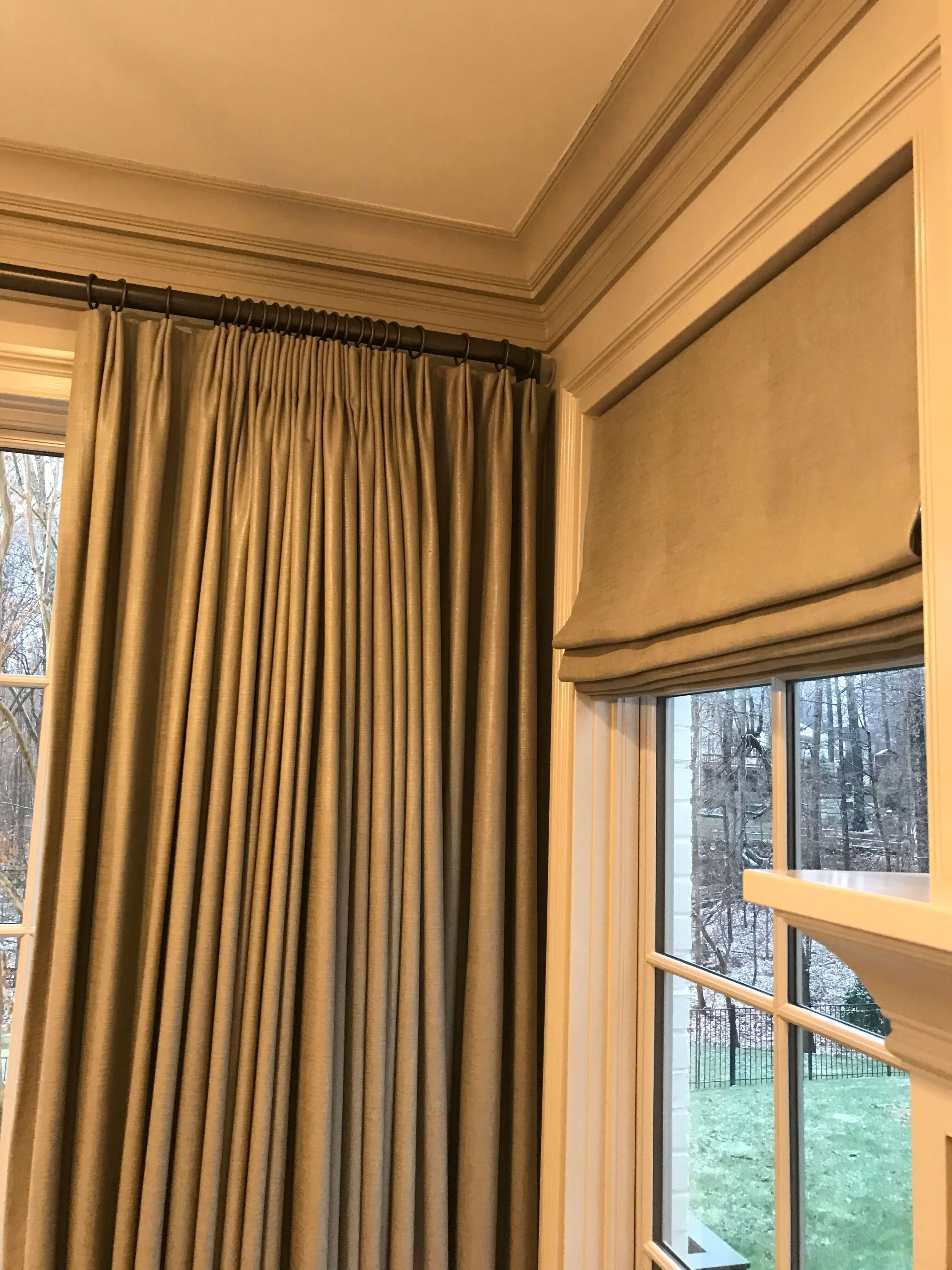 An up-close photo of two operational linen drapery panels mounted on a metal rod and a Roman shade that is mounted on a board.
